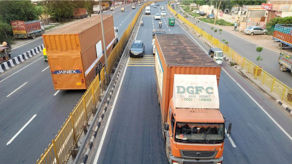 Two large, orange goods carrier trucks on a highway in India